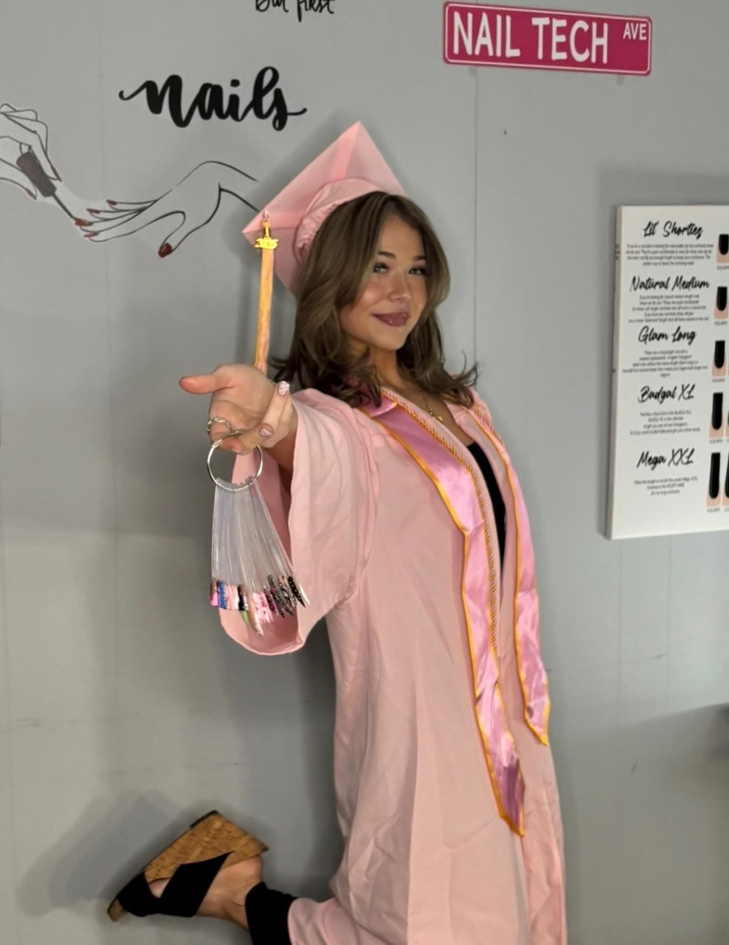 Nail tech graduate in pink gown with graduation prop